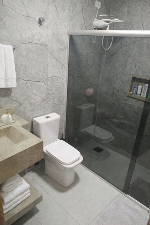 Et moderne badeværelse med marmorvæg, bruseniche med glasvæg, toilet og vaskebord med vask og håndklædestang.