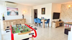 Ein modernes Wohnzimmer mit einer Fußballstoßmaschine, einem Essbereich mit blauen Stühlen und einem Fernseher auf einem Holzboden.