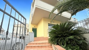 A building with a yellow facade, a green door, and a staircase leading to a balcony. - L'Ostro - Civitanova Marche, new two-room apartment in a strategic location (Civitanova Marche)
