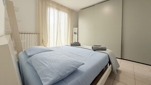 A modern bedroom with a bed, a radiator, a window with curtains, and a wardrobe. - L'Ostro - Civitanova Marche, new two-room apartment in a strategic location (Civitanova Marche)