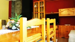 A wooden dining table with chairs, a floral centerpiece, a cabinet with glass doors, and a television set. - Turisme Rural El Janpere - La Cabanya (Sant Joan de les Abadesses)