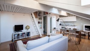 Eine moderne Loftwohnung mit weißem Sofa, Essbereich, Küche und einer Treppe zu einer erhöhten Ebene.