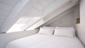 Ein Schlafzimmer mit schrägen Wänden, weißen Wänden und einem Bett mit weißer Bettwäsche.
