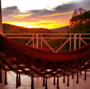 Una hamaca en un balcón con vistas a una puesta de sol sobre un paisaje montañoso.