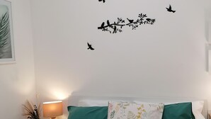 Una camera da letto con un letto, due cuscini, un comodino con una lampada e decorazioni murali raffiguranti uccelli e rami.