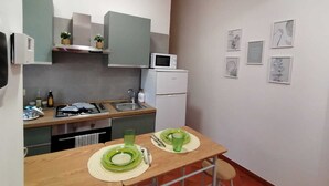 Angolo cottura compatto con microonde, lavandino e una piccola zona pranzo con tavolo apparecchiato per due persone.