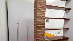 Una stanza con una parete decorata in mattoni, un armadio bianco e una scaffalatura in legno.