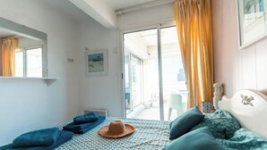 A bedroom with a bed, a window with curtains, a door leading to an outdoor area, and a small table with a chair. - Terrasses Catalanes Sea&Mountain View near the beach & private parking (Canet-en-Roussillon)