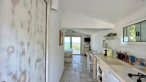 A kitchen with a stone floor, a large window, and a view of the sea. - Ostuni Green Hills Apt. 1 – Charming Home with Panoramic View & Shared Jacuzzi (Puglia)