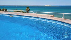 Una piscina con acqua cristallina, un bordo piastrellato e vista sul mare e sulla costa in lontananza.