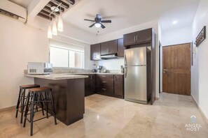 A modern kitchen with dark cabinets, a stainless steel refrigerator, a microwave, and two bar stools. - Oceanview Balcony, RoofPool, Steps to Malecon (La Paz)
