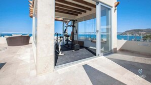 Una palestra con attrezzature, una porta in vetro e vista sul mare.