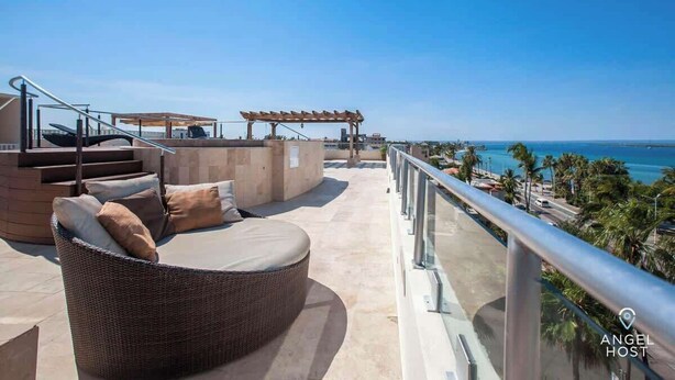 Una terrazza sul tetto con un divano in vimini, un pergolato e vista sul mare.