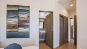 A hotel room with a bed, a painting of boats on the wall, a bathroom with a sink, and a staircase. - Exclusive Residential Living at Puerta Cortes (Lomas de Palmira)