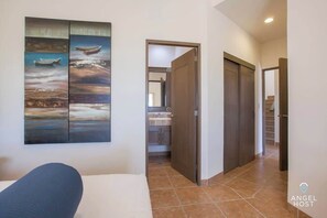 A hotel room with a bed, a painting of boats on the wall, a bathroom with a sink, and a staircase. - Exclusive Residential Living at Puerta Cortes (Lomas de Palmira)