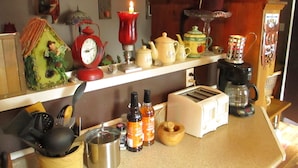 Una cocina con diversos electrodomésticos y adornos, incluyendo un reloj rojo, una tetera y una pequeña figurita en la encimera.