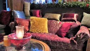 Una sala de estar acogedora con un sofá mullido decorado con varios cojines, una mesa de vidrio con una vela y un cuenco decorativo.