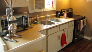 Cocina compacta con lavamanos, estufa y ventana con persianas.