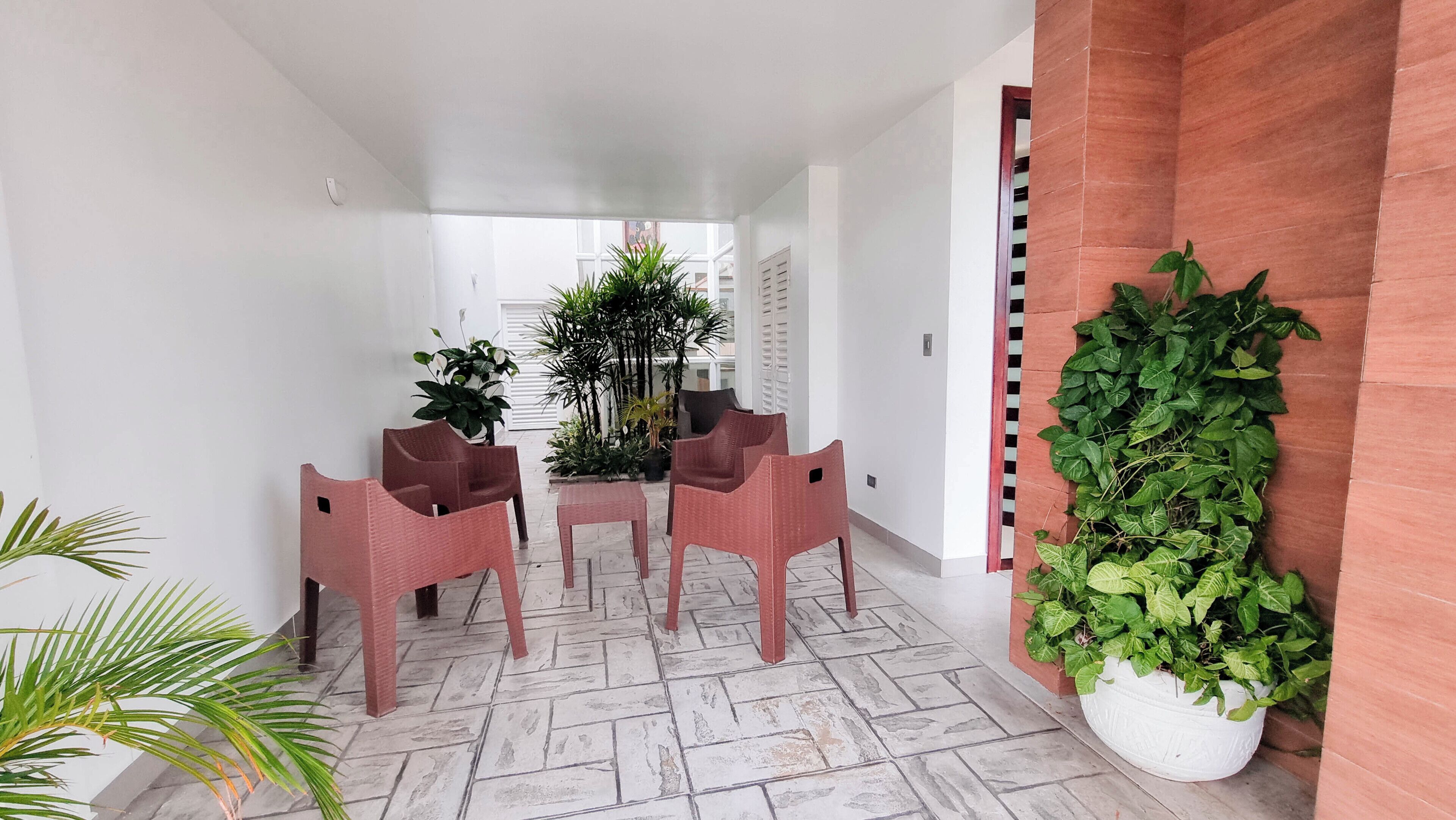 A hallway with a tiled floor, a seating area with chairs and a table, and potted plants.