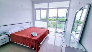 Un dormitorio con cama, mesita de noche, cómoda y una ventana grande con vistas a zonas verdes.