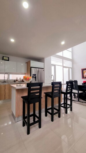 A modern kitchen with a central island, bar stools, stainless steel appliances, and a large window providing natural light. - Terrazas Merida Lodge (Mérida)