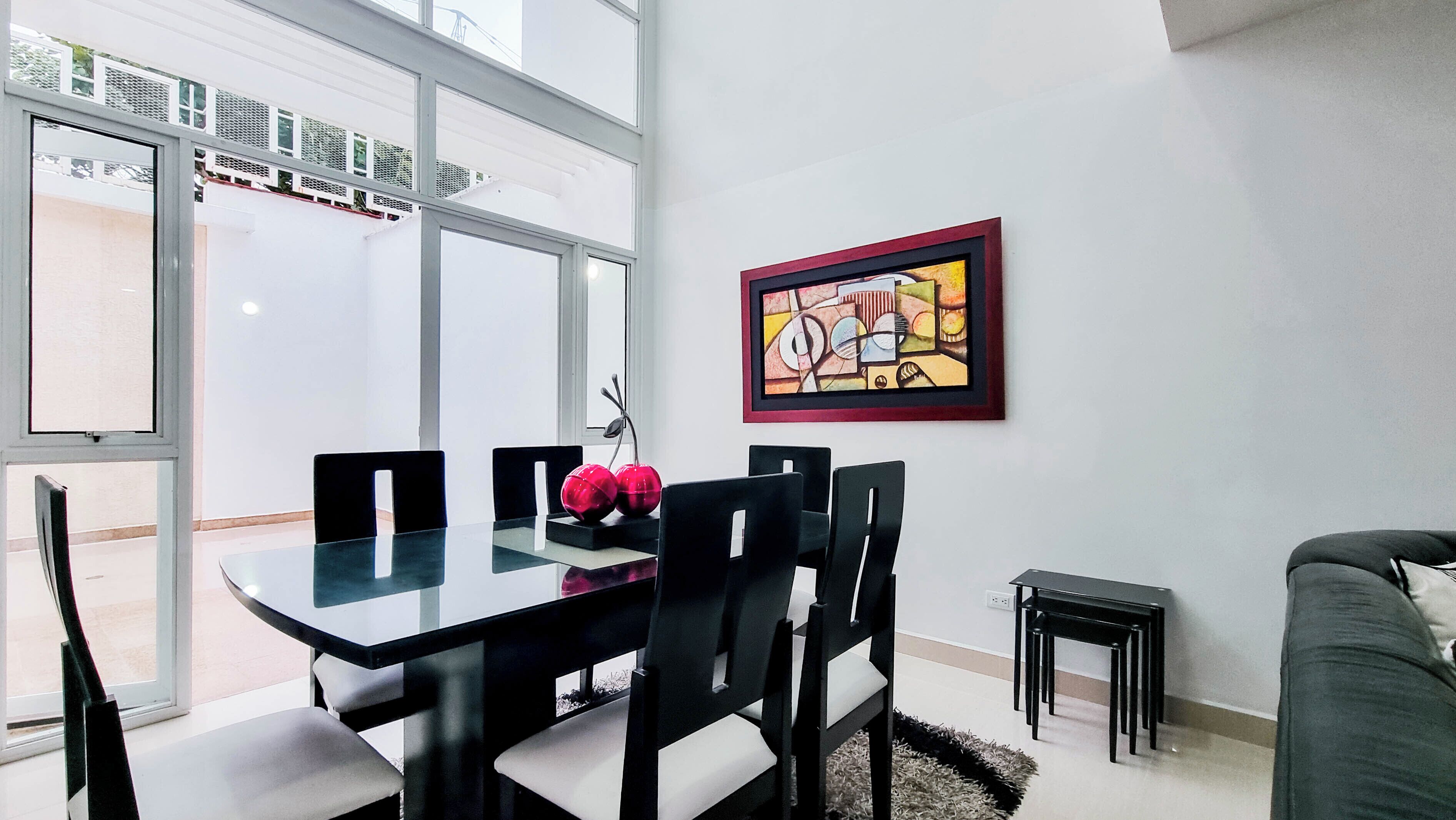 A dining area with a glass table, black chairs, and a red decorative item.