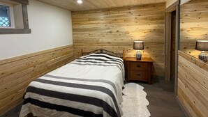 Une chambre avec un plafond en bois, un lit recouvert d’une couverture à rayures, une table de chevet avec une lampe et une fenêtre donnant sur un beau paysage.
