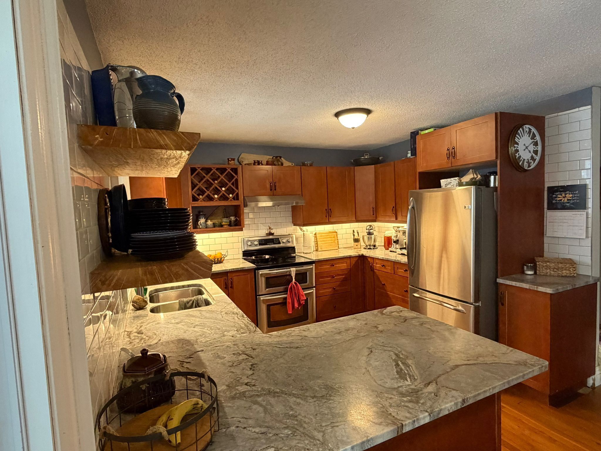 Una cocina con gabinetes de madera, un refrigerador de acero inoxidable, un horno empotrado y una encimera de mármol.