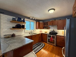 Una cocina con armarios de madera, un refrigerador de acero inoxidable, un horno doble y una ventana sobre el fregadero.