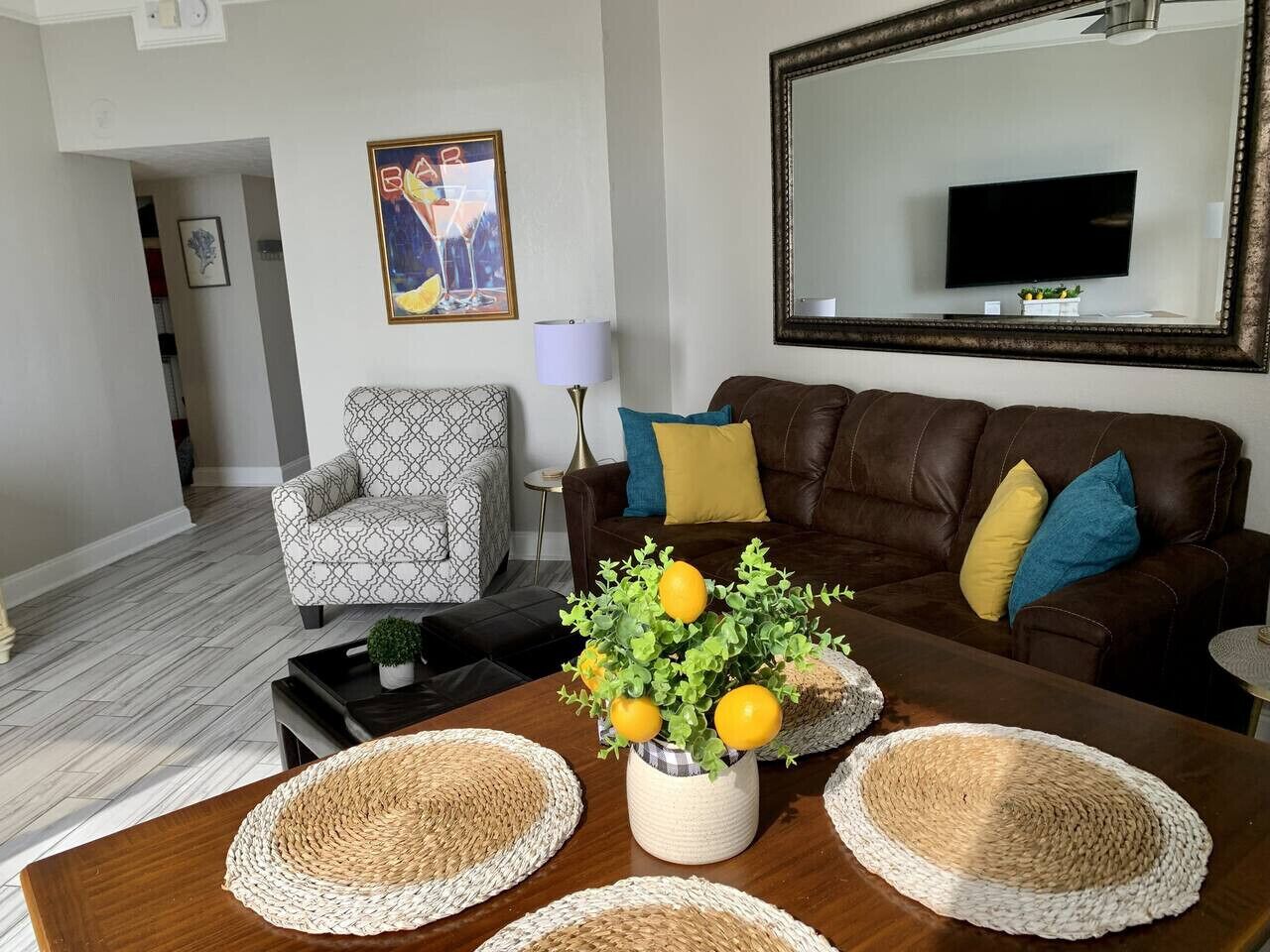 A living room with a brown leather sofa, patterned armchair, and a coffee table with woven placemats and a vase of lemons.