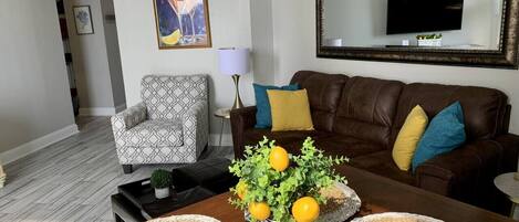 A living room with a brown leather sofa, patterned armchair, and a coffee table with woven placemats and a vase of lemons.