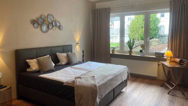 Ein Schlafzimmer mit Bett, Nachttischlampen, einem Fenster mit Vorhängen, einem Heizkörper und Wanddekoration.