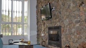 A living room with a stone wall, a fireplace, a mounted TV, and a round glass coffee table. - Rural house in the middle of nature (Chiclana de la frontera)