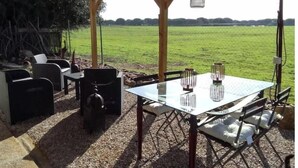 An outdoor patio with a table and chairs, a hanging lantern, and a view of a green field. - Rural house in the middle of nature (Chiclana de la frontera)