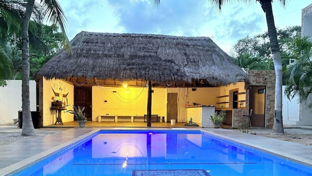 A pool area with a thatched-roof structure, a lounge area, and a stone wall. - Luxury Studio & 1BR Condos • Pools • Near Tulum & Akumal Beaches (Akumal)
