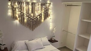 A modern bedroom with a large bed, a wall-mounted light fixture, and a white wardrobe. - Luxury Studio & 1BR Condos • Pools • Near Tulum & Akumal Beaches (Akumal)