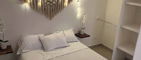 Une chambre moderne avec un grand lit, un luminaire fixé au mur et une armoire blanche.