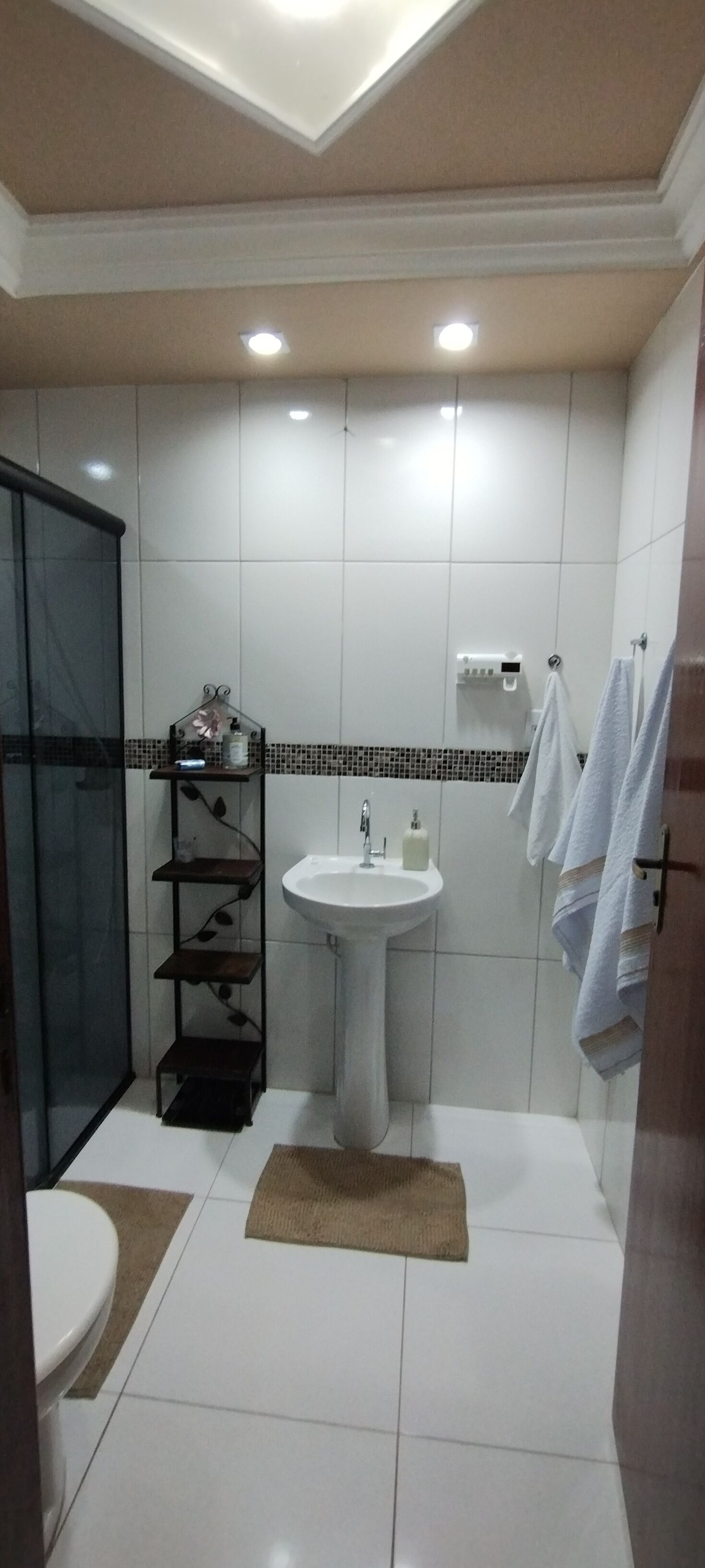 Un baño con un lavamanos blanco, cabina de ducha de cristal y un estante con artículos de aseo.