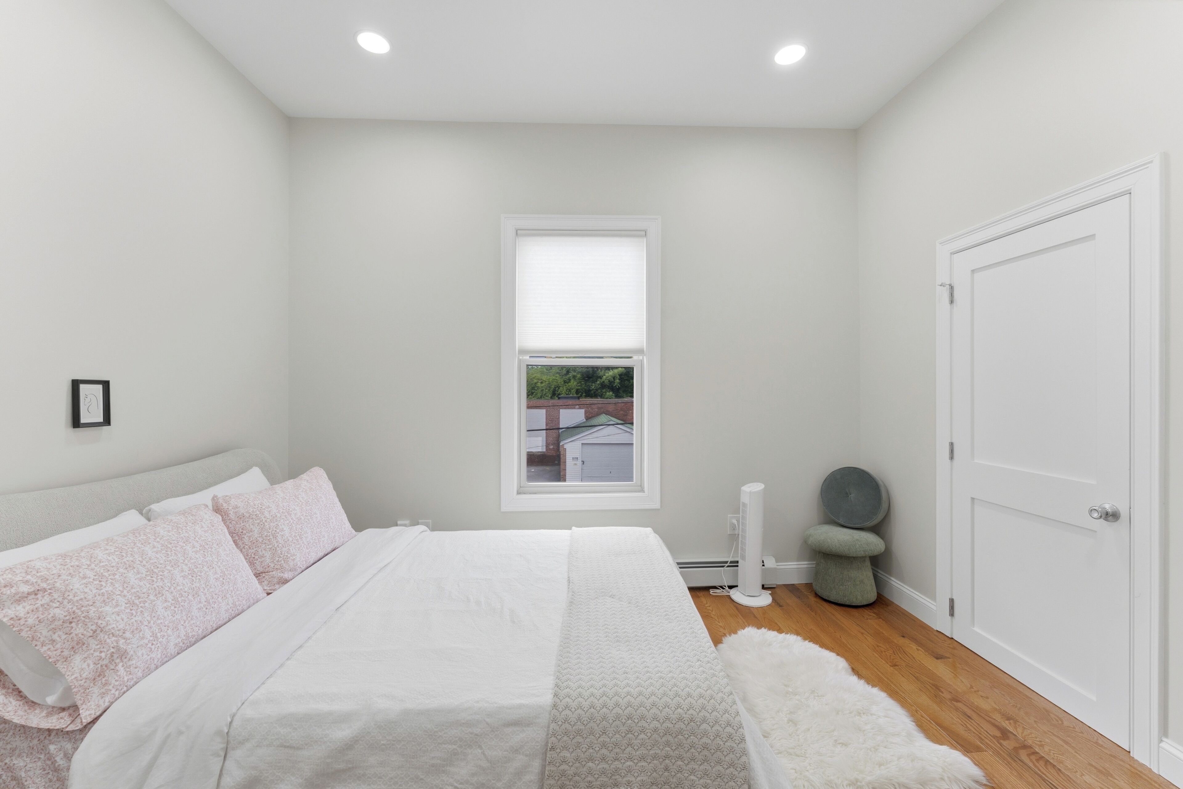 Un dormitorio con cama, ventana, puerta y un taburete pequeño.