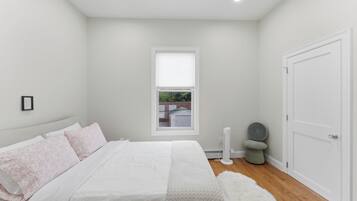 Un dormitorio con cama, ventana, puerta y un taburete pequeño.
