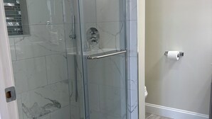 A glass-enclosed shower with a marble-tiled wall, a metal handle, and a toilet paper holder on the adjacent wall. - Broadway Nomad House in Providence (Providence)