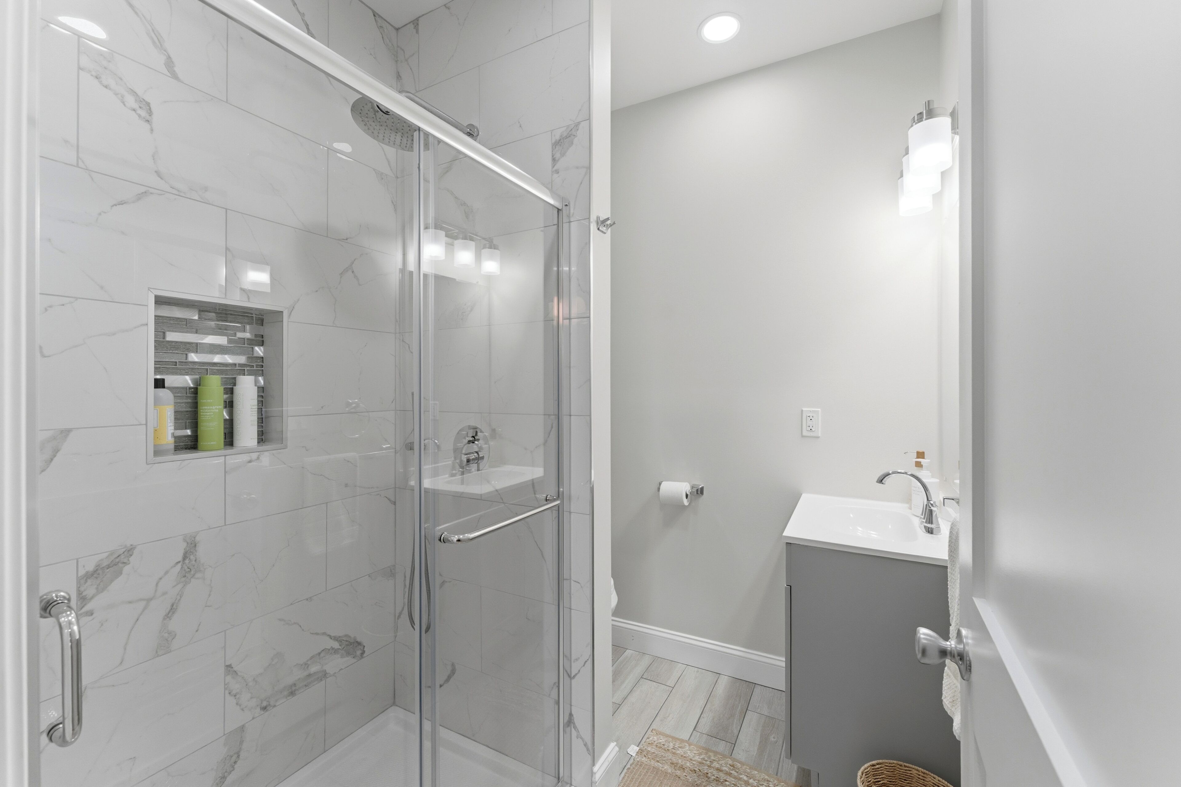 A modern bathroom with a glass-enclosed shower, a vanity with a sink, and a mirror.
