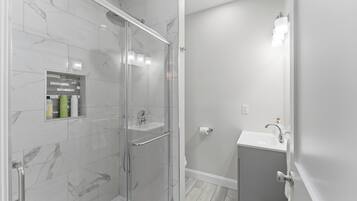 A modern bathroom with a glass-enclosed shower, a vanity with a sink, and a mirror.