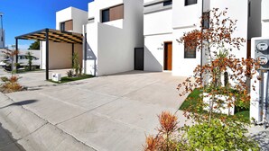 Um edifício moderno com fachada plana, área externa coberta e um pequeno jardim.