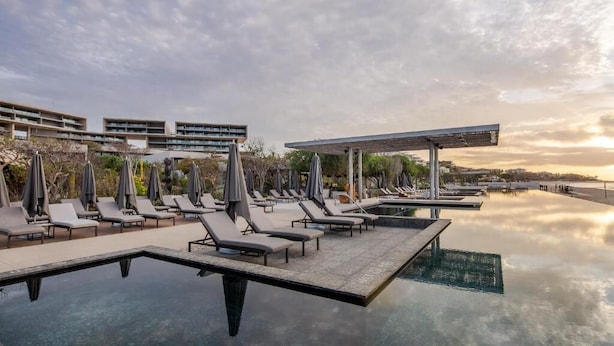 Une piscine à débordement située sur le toit, agrémentée de chaises longues et de parasols, et entourée d’immeubles modernes.