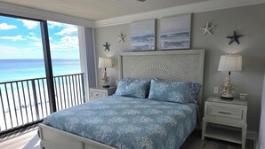 Een slaapkamer met een bed, nachtkastjes, een plafondventilator, decoraties met zeesterren en uitzicht op de oceaan.
