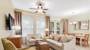 Un salon comprenant un ensemble de canapés, une table basse, un téléviseur, un ventilateur de plafond et un coin repas avec une table et des chaises.