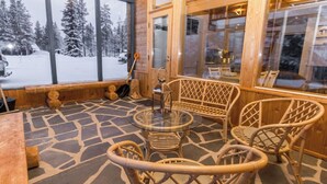 A cozy wooden cabin interior with a stone floor, wicker furniture, and large windows offering a snowy forest view. - Lupponen by Interhome (Inari)