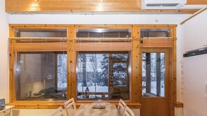 A wooden interior with a dining table and chairs, large windows with blinds, and an air conditioning unit. - Lupponen by Interhome (Inari)