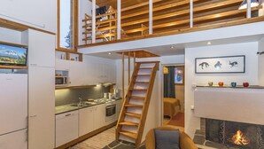 A modern loft-style living space with a kitchen, a fireplace, and a loft area with a wooden staircase. - Lupponen by Interhome (Inari)